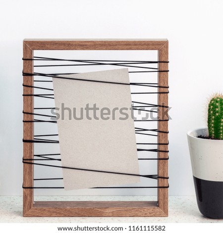 Wooden frame with a gray mockup with a cactus in a pot on the right standing on a table with terrazzo on a white wall