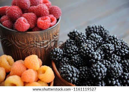 Raspberries are black, yellow and red in clay ware on a wooden table. View from above.
 Royalty-Free Stock Photo #1161119527