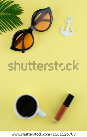 Sungalsses, lipsticks and coffee decorate with fern leave and tiny anchor on yellow background with copy space