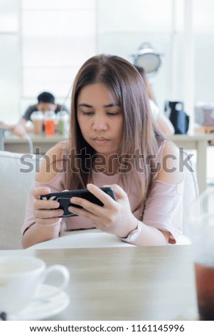 Portrait of an Asian woman sitting and using the internet from a smartphone in a coffee shop.