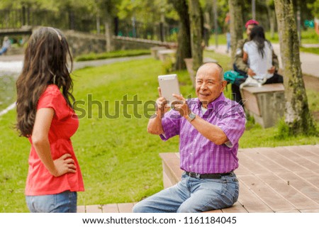 Outdoor view of father taking pictures with a tablet to his daughter in the park