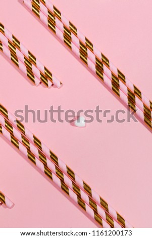 Spiral pink & gold disposable drinking straws in an array along with white hearts, against pink background.