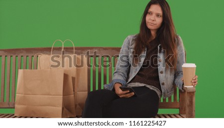 Portrait of girl sitting on bench with shopping bags and phone on green screen