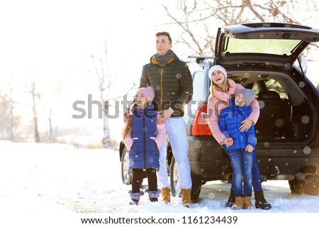 Happy family near car outdoors during snowfall. Winter vacation