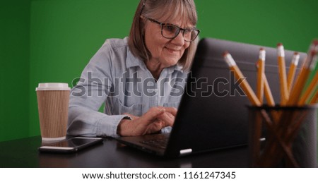 Portrait of smiling old woman in office using laptop on green screen