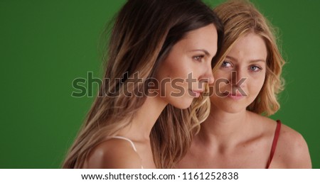 Pretty blonde girl looking at camera while friend look offscreen on green screen