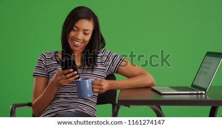 Smiling black woman with coffee using mobile device at cafe on green screen