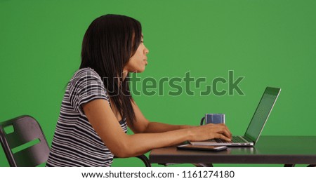 Side view of black woman working on laptop computer at table on green screen