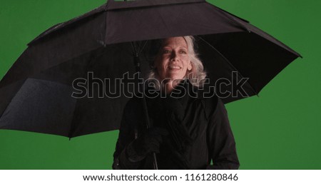 Charming old woman standing in the rain with umbrella on green screen