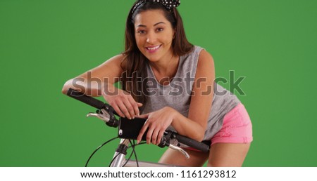 Beautiful Latina posing on bicycle with smartphone on green screen