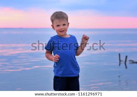 Smiling toddler boy with amazing pink sea sunset on background