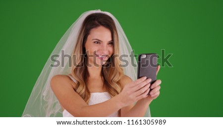 Lovely young bride taking selfie with smartphone on green screen