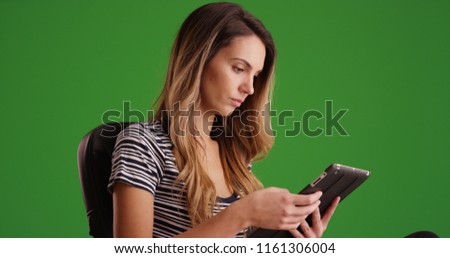 White millennial woman working on tablet sitting in office chair on green screen