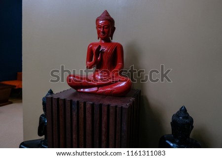 a statuette of a red Buddha in a lotus pose against a wall