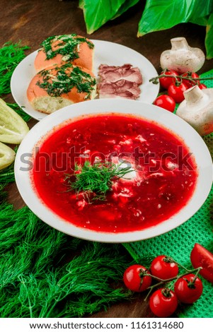 borscht, fat and pampushki in a white plates among vegetables and greenery on a wooden table with a green napkin. close-up. top view. series of photos