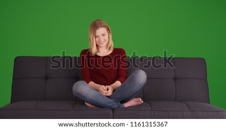 Casual young blonde woman sitting on sofa smiling on green screen