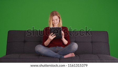 Millennial relaxed on sofa browsing internet with digital tablet on green screen