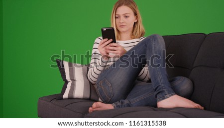 Portrait of millennial girl relaxing on couch using cellphone on green screen