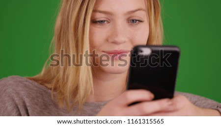 Pretty millennial girl using smartphone to send text messages on green screen