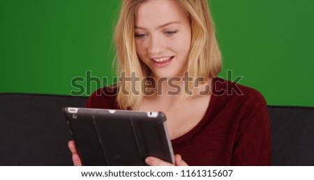 Casual blonde woman in her 20s using tablet sitting on couch on green screen