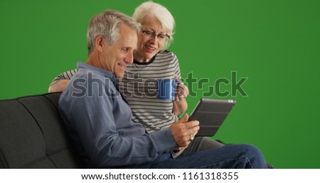 Modern senior couple sitting on couch with tablet on green screen