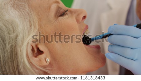 Dentist examining elderly woman's teeth during checkup on green screen