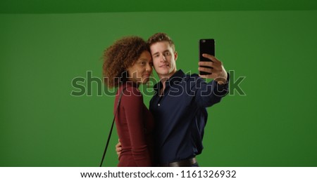 Happy interracial couple using smartphone to take selfie on green screen