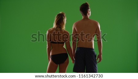 Rear view of young white couple in swimsuits holding hands on green screen
