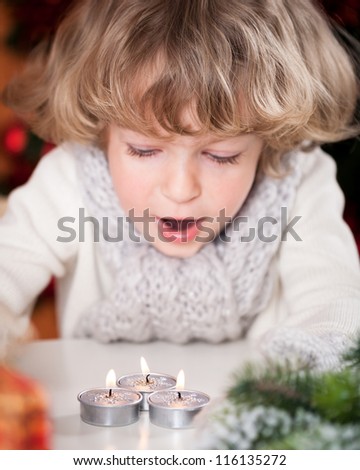 Beautiful child blowing out burning Christmas candles. Focus on candles