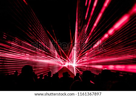 Red laser show nightlife club stage with party people crowd. Luxury entertainment with audience silhouettes in nightclub event, festival or New Year's Eve. Beams and rays shining colorful lights