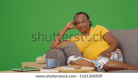 Cheerful old black woman smiling at camera on her sofa on green screen