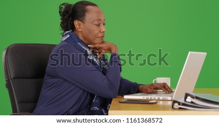 A black businesswoman uses a laptop at her desk on green screen