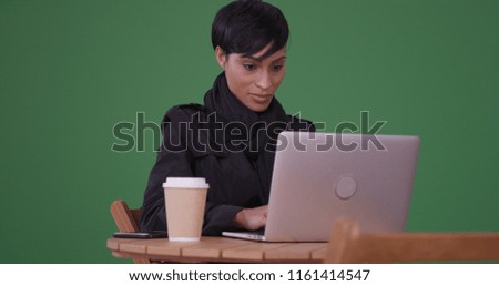 Fashionable woman using laptop computer at a cafe table on green screen