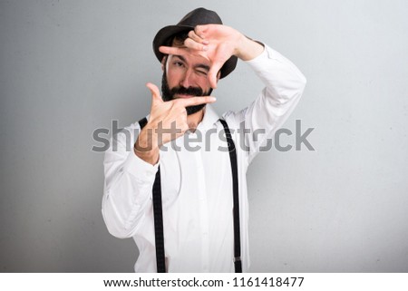 Hipster man with beard focusing with his fingers on grey background