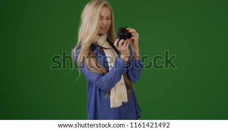 Young white girl in a scarf takes a picture with her camera on green screen