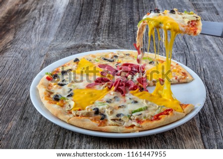 Hot pizza slice with melting cheese on a rustic wooden table.