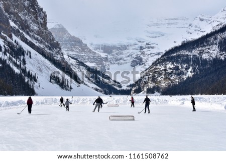 Group of people playing hockey on a frozen lake in Canada with glacier in the background
