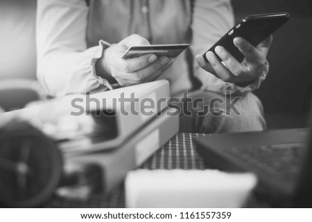 Woman in casual shirt paying with credit card online while making orders via the Internet. Successful businesswoman making transaction using mobile bank application. Black and white picture.