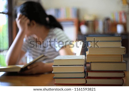 Close-up of several books stacked on a table in a library. The girl is reading a tired book as a background selective focus and shallow depth of field
