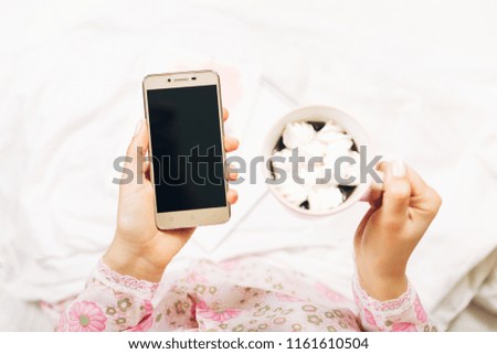Girl with smart phone and coffee in her hands.Working at home,in bed.Top view