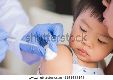 Doctor giving an injection vaccine to a girl. Little girl crying with her mother on background.