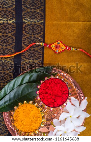 Indian Festival: Rakhi with rice grains, kumkum, sweets and haldi on plate with an elegant Rakhi. A traditional Indian wrist band which is a symbol of love between Brothers and Sisters