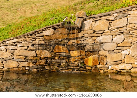 Small waterfall in national park. Stone wall in landscape.