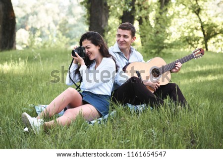 young couple walking in the forest and playing guitar, taking photo on old camera, summer nature, bright sunlight, shadows and green leaves, romantic feelings