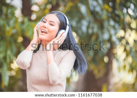 Asian young woman relax and listening music with headphone in the nature green park, happy time.
