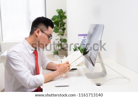 Happy businessman with book in hand looking at computer monitor in office