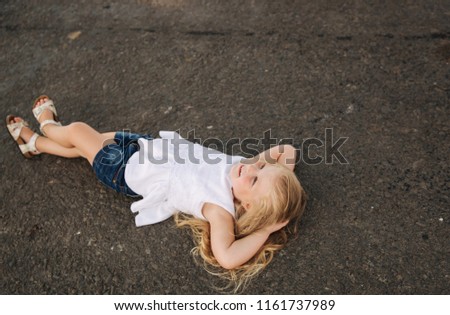 Little girl lie on the road near big alley