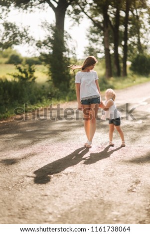 Mother and little daughter walk though the alley and hold each others hands. Shadow on the road
