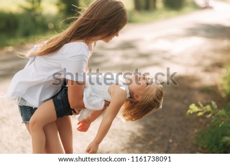little girl playing with mom in the park in summer day during the sunset