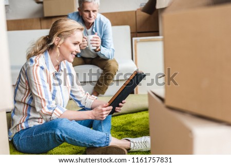 happy elderly woman holding photo album while relocating with husband in new house 